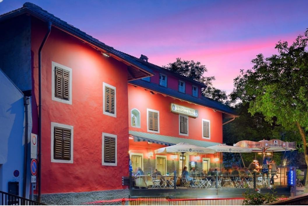 The charming exterior and summer terrace of Bierstube Oberweger, a traditional Tyrolean inn in Kollmann, South Tyrol.